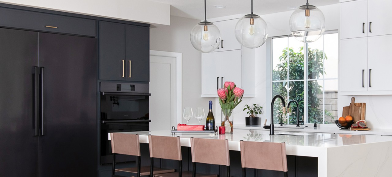 Modern kitchen with black refrigerator, white marble island, and glass globe pendant lights.