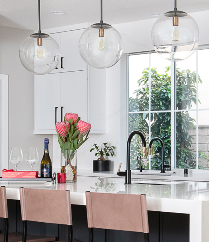 Modern kitchen with black refrigerator, white marble island, and glass globe pendant lights.